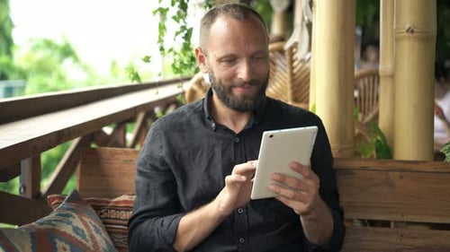 Young, Happy Man Surfing Internet On Tablet Sitting In Cafe