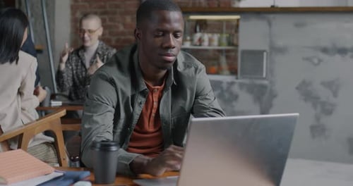 Ehrgeiziger afroamerikanischer Unternehmer, der mit Laptop arbeitet und lächelt im Café