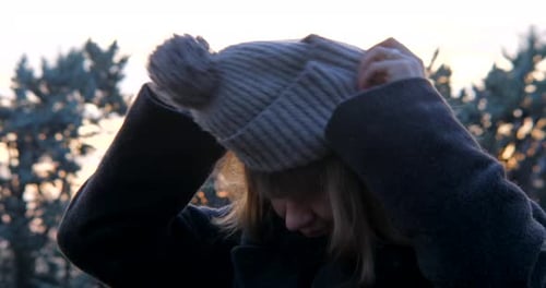 Woman Puts On Hat Outside at Sunset