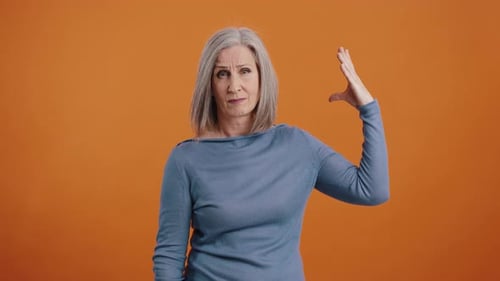 Mature Woman Gesturing Hand on Orange Background