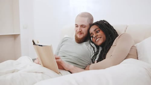Loving Couple Reading Together in Bed at Home