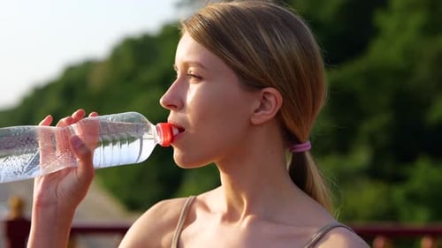Woman Drinks Water on a Bridge in Sunlight