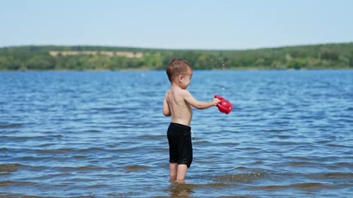 Small funny child playing on river with water. Summer sunny day and splashing on a beach.