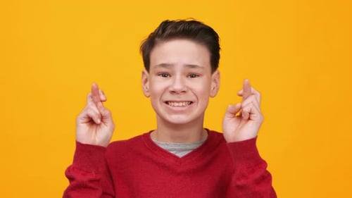 Teen Boy Smiles Crossing Fingers on Bright Background
