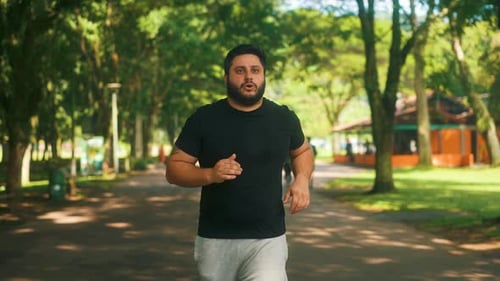 Focused overweith guy jogging outdoors at a park