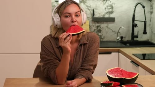 Woman Enjoying Watermelon Slice While Wearing Headphones
