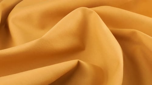 Top view of the soft folds of topaz orange cotton fabric rotated on the display case.