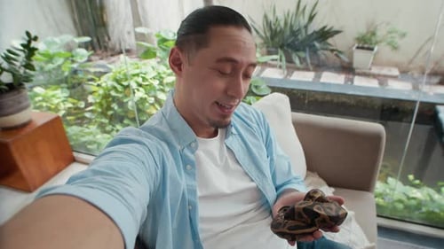 POV d'un homme bloguant devant la caméra en train de caresser un serpent python à la maison