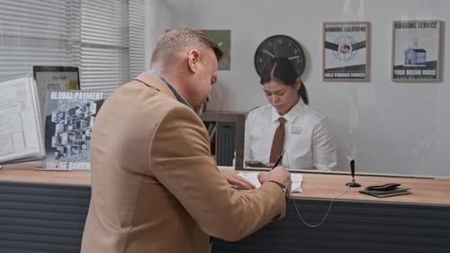 Portrait of Man Signing Documents, While Bank Teller Working Intently Behind Him