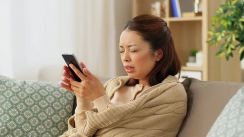 Woman on Couch Looks Concerned at Smartphone