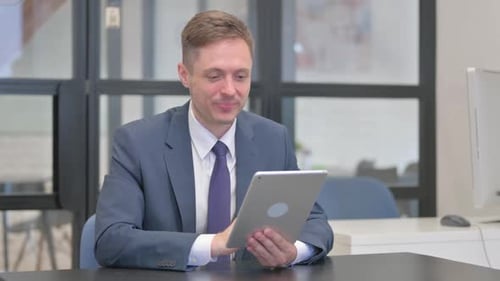 Mature Adult Businessman Doing Video Chat on Tablet in Office