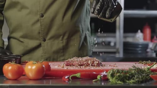 Chef seasoning steak in commercial kitchen