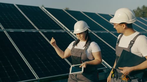 Workers in Overalls Walk Around the Solar Panel Area and Analyze Data