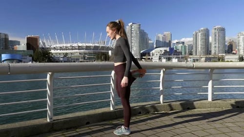 Young athletic woman stretching hamstrings before morning run in metropolitan area