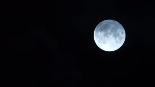 Full moon glowing with clouds moving past blown by wind, black background, night