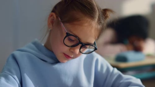 Closeup Pensive Girl in Eyeglasses Learning at School Class. Thoughtful Student Writing