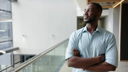 Smiling businessman standing confidently with arms crossed in modern office hallway, copy space