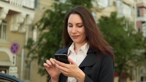 Woman in a Business Suit Stands on the Street Street and Uses Smartphone