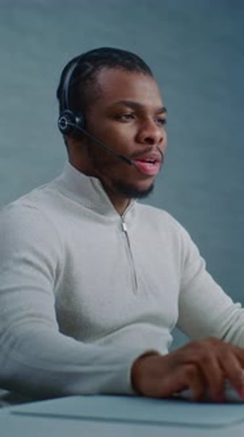 African American Hotline Operator Talks on Headset with Customer Works on Computer