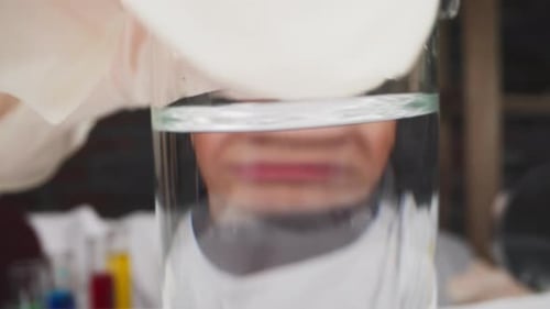Un travailleur portant des gants place un bécher contenant du liquide devant la caméra