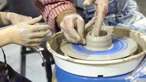 Child Learning Pottery from Adult on Wheel