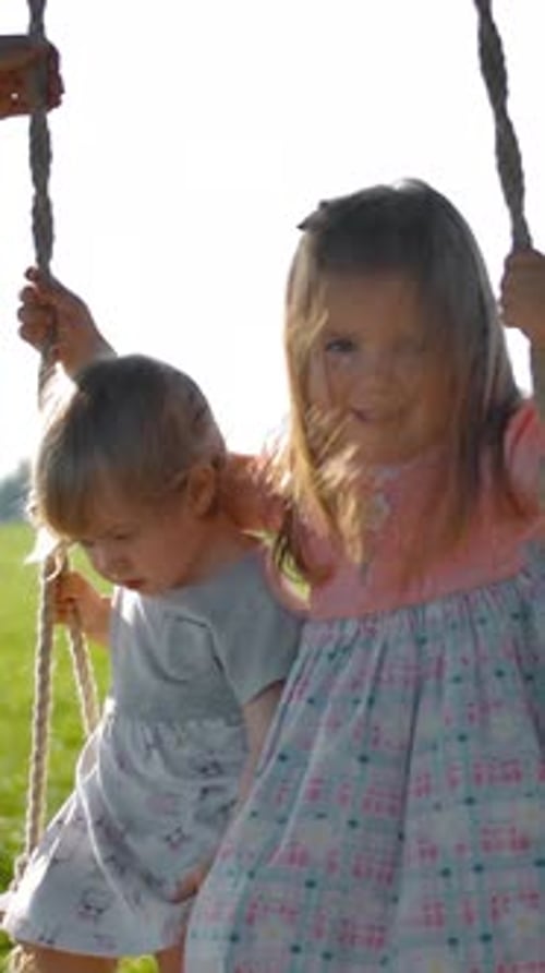 Two Young Girls Swinging Together in Sunlit Field