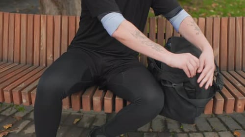 Individual Searches Through Backpack Person on Park Bench Preparing Belongings Man with Tattooed