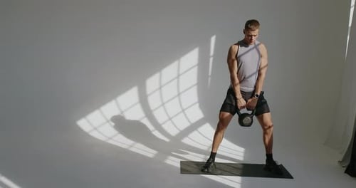 Man Doing Kettlebell Squats in Bright Studio