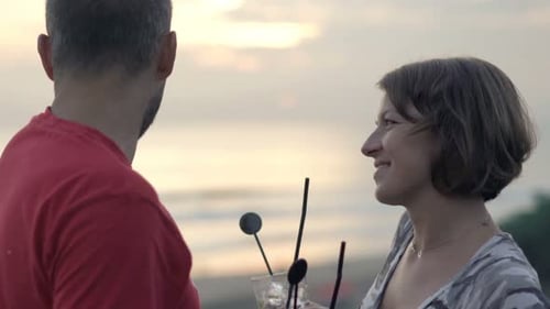 Young couple enjoying cocktails and a romantic sunset view on a balcony