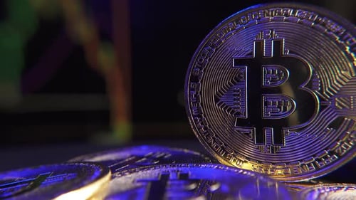 Shiny bitcoin on blurred background with moving red and green candlesticks