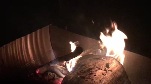 Plan filmé à main levée d'une grosse bûche brûlée dans un foyer géant, la nuit
