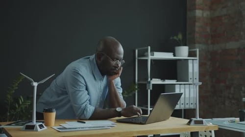 Black Engineer Working on Sustainable Energy Project on Laptop at Office Desk