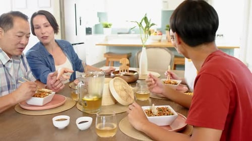 Family Gathering Around Table Eating Asian Noodles