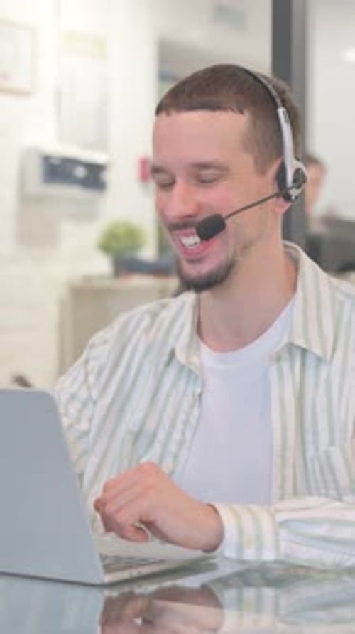 Creative Young Man with Headset Doing Video Chat on Laptop in Call Center, vertical video