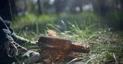 Un hombre con una bolsa de plástico recoge una botella de vidrio que está tirada en el césped mientras recoge basura en el