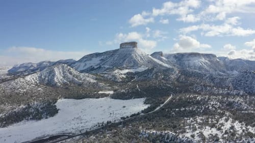 Drone footage shows a road travelling over snow capped mountain range with a razor sharp peak covere