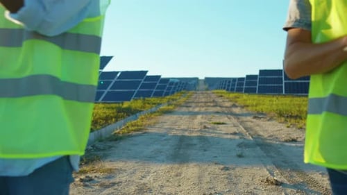 Moving Backwards Engineers with Laptop on the Solar Farm in Special Uniform Standing Discuss the