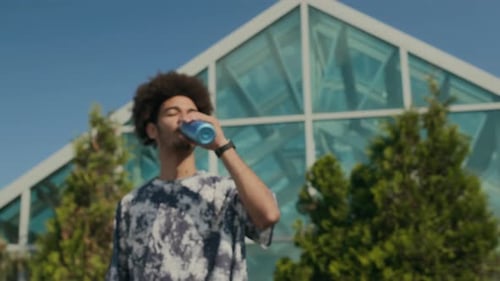 Portrait of Young Man Drinking Water Outdoors after Street Workout