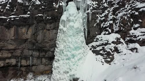 Vista aérea de una cascada helada congelada y un acantilado cubierto de nieve en un paisaje montañoso, foto de un Zumbido dolly