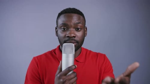 Engaging Man Speaks Into Microphone, Grey Background
