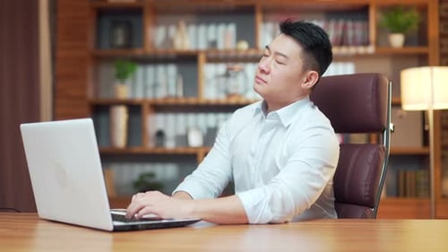 Exhausted, overworked asian office worker sitting in the office with a headache massaging head.