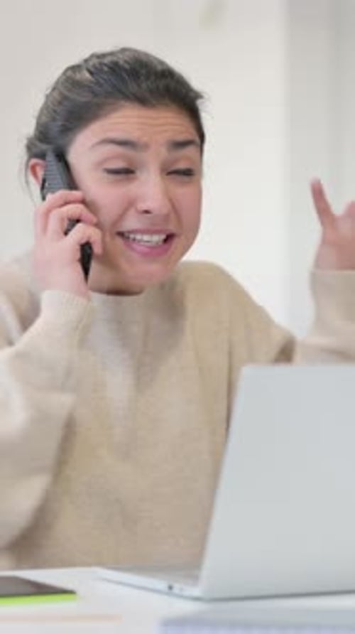 Frustrated Woman Talking on Phone by Laptop