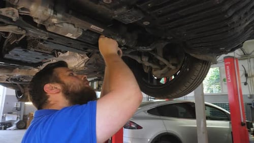 Jeune mécanicien automobile inspectant la suspension d'une voiture au garage