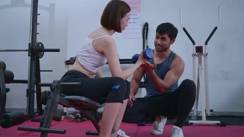 Young couple exercising in a gym When lifting weights, they assist one another