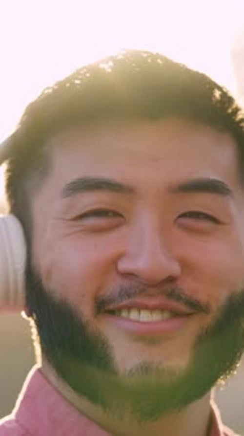 Asian Man Listening to Music with Headphones Smiling to the Camera Outdoors