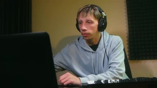 Young Music Producer with Headphones Working at a Home Studio on a Laptop