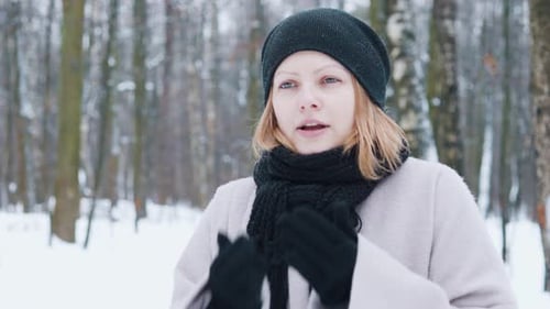 Winter Girl Rubs Blows on Hands to Warm Up While Walking in Park Snowy Forest