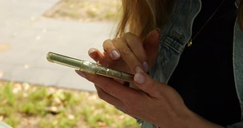 Woman Holds Smartphone Typing and Scrolling on Screen with Fingers Outdoors