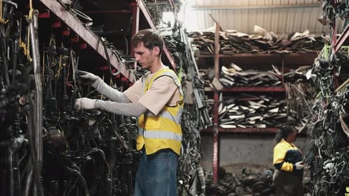 White male worker checks auto spare parts stock storage at stack warehouse.