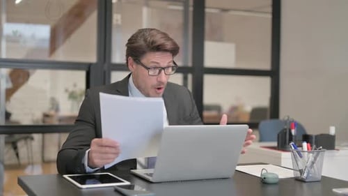 Businessman Viewing Documents at Office Desk Looking Frustrated